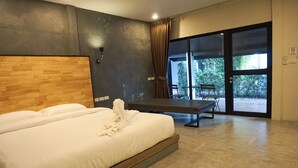 Un dormitorio moderno con una cama grande, cabecera de madera, un banco y un ventanal corredero que da a un área exterior con un banco y árboles.