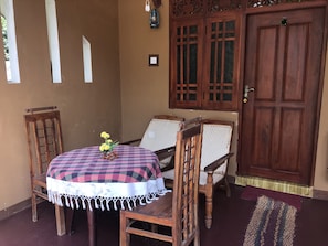 A wooden table with a checkered tablecloth, two wicker chairs, and a vase with yellow flowers.