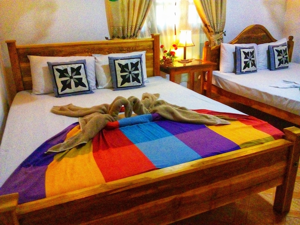A hotel room with a wooden bed, a bedside table with a lamp, and a small table with flowers.