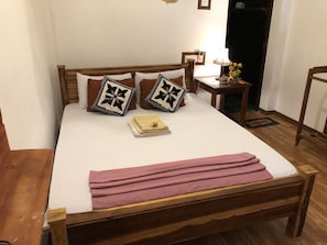 A wooden bed with white bedding, two decorative pillows, a bedside table with a lamp, and a small vase with flowers.