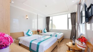 A hotel room with two beds, a wooden desk, a chair, a TV mounted on the wall, and a window with curtains. - Khach San Novena (Ho Chi Minh City)