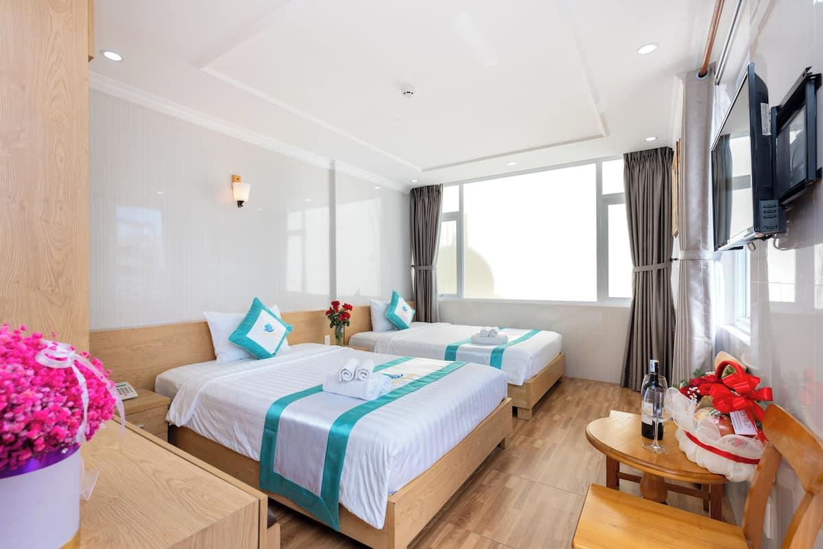 Hotelkamer met twee bedden, een houten bureau, een stoel, een aan de muur bevestigde televisie en een raam met gordijnen.