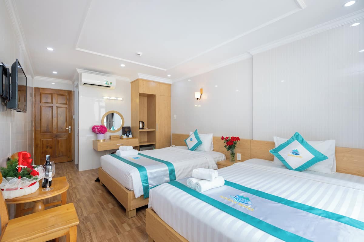 Een hotelkamer met twee bedden, een houten garderobe, een tafeltje met fles en glas, en een aan de muur bevestigde televisie.