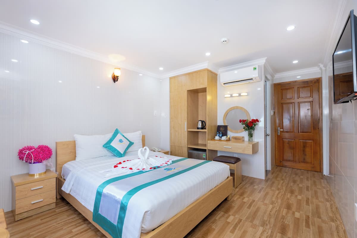 Een hotelkamer met een groot bed, een houten vloer, een bureau met stoel, een kaptafel met spiegel en een aan de muur bevestigde televisie.