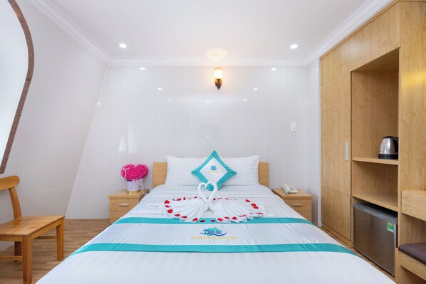 A hotel room with a bed, a nightstand, a desk, a chair, a wardrobe, and a refrigerator.