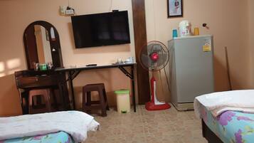 Una habitación con dos camas, un escritorio, un televisor, un ventilador, un refrigerador y un espejo.