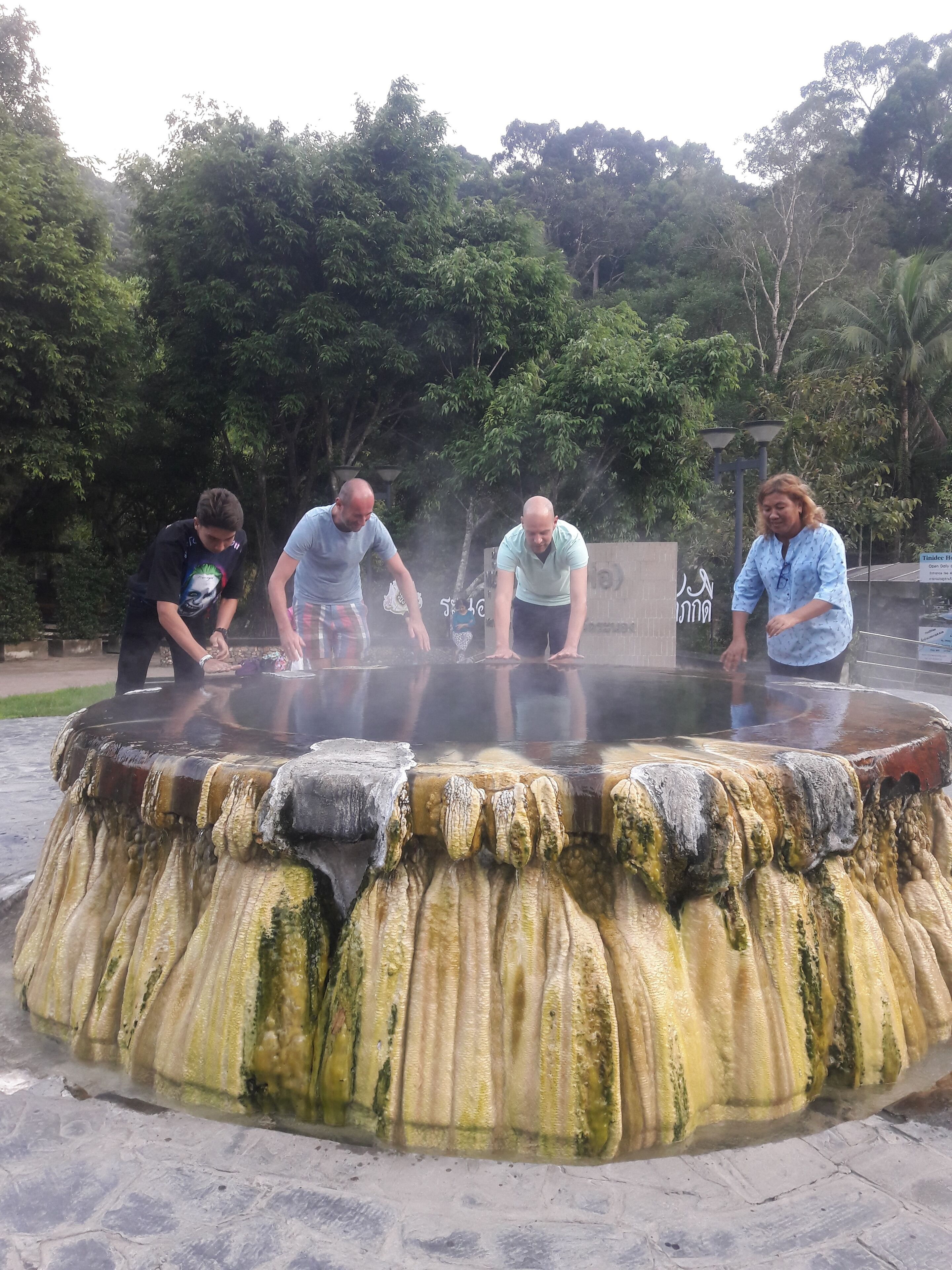 A group of people around a hot spring with a stone basin and a sign in the background.