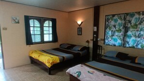 Una habitació amb dos llits individuals, un finestral gran, una làmpada penjada a la paret i un quadre amb temàtica tropical.