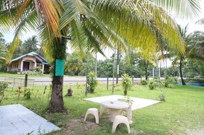 A small outdoor seating area with a table and two stools, surrounded by lush greenery and palm trees.