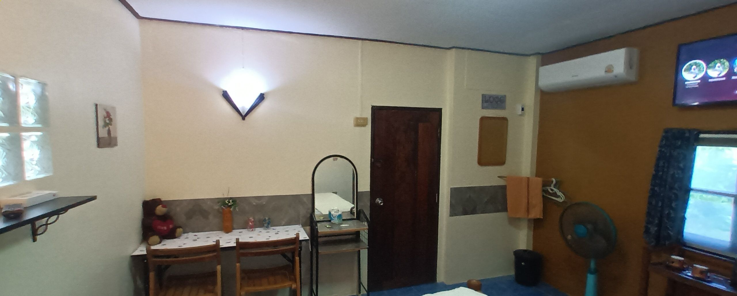 A room with a dining table, chairs, a mirror, a small shelf, a door, and a wall-mounted air conditioner.