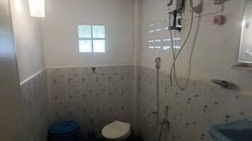 Baño pequeño con inodoro, lavamanos y ducha. Cuenta con una ventana que proporciona luz natural.