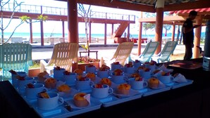 Un espacio cubierto al aire libre con mesas dispuestas para el desayuno, con vista a una playa.
