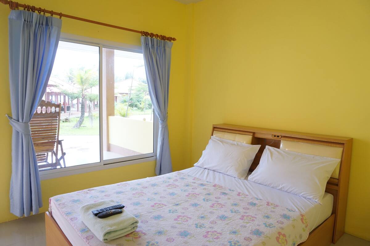 A bed with a floral bedspread, a remote control, and a towel on a wooden nightstand.