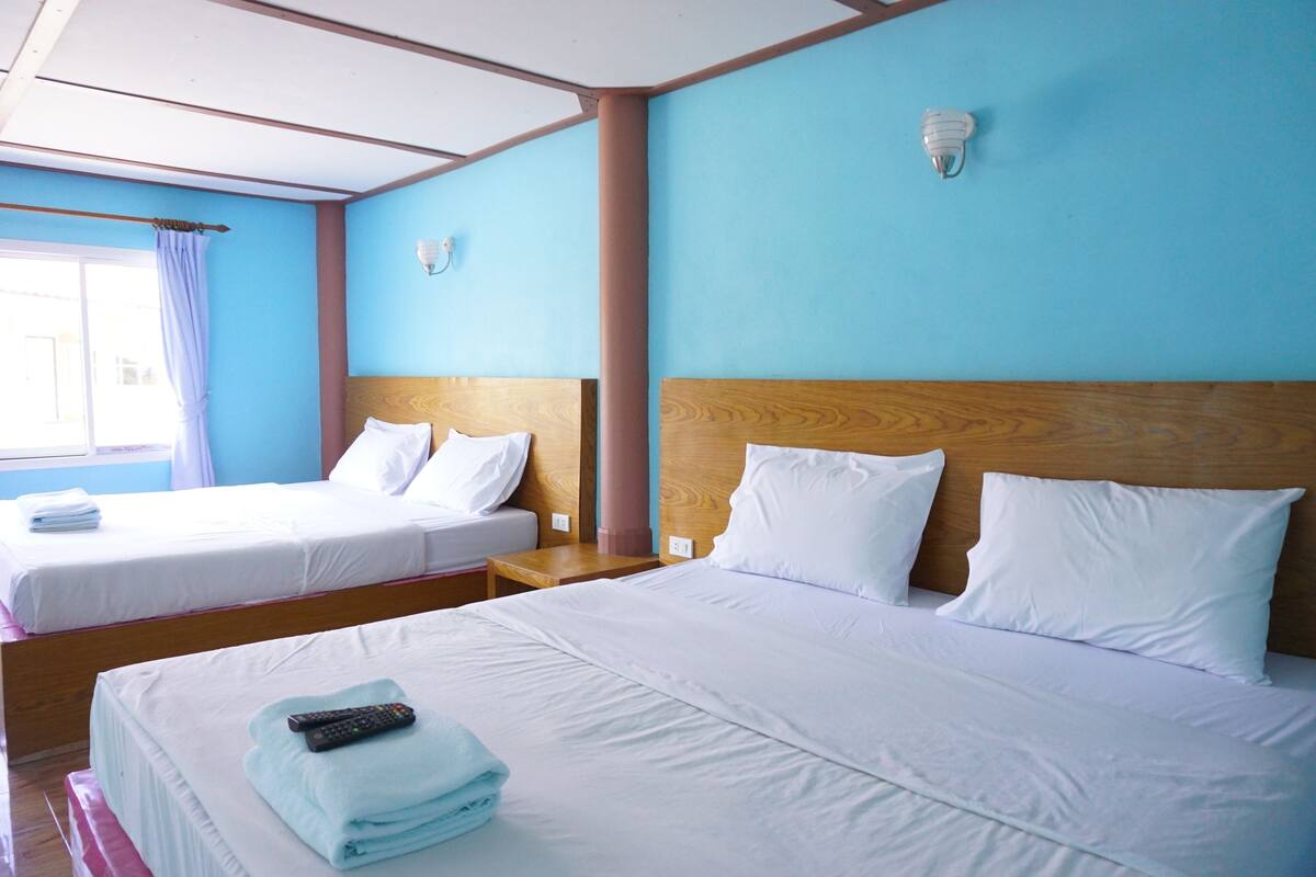 A hotel room with two beds, wooden headboards, white bedding, a remote control, and a window with curtains.
