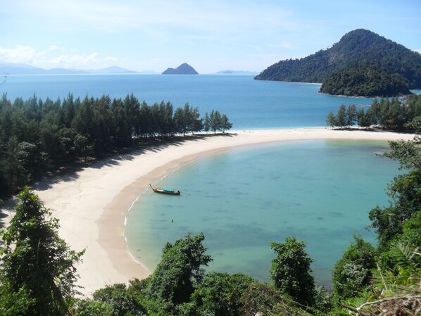 A beach with clear turquoise waters, a boat on the shore, and a forested area.