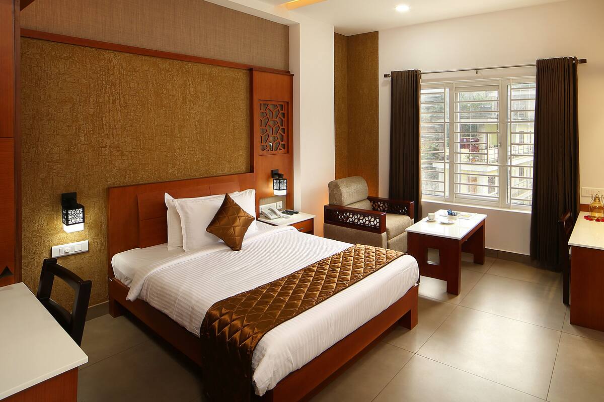 A hotel room with a large bed, a desk, a chair, a nightstand, and a window with curtains.