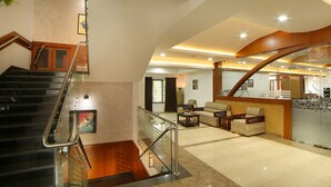 A hotel lobby with a staircase, seating area, and a reception desk. - Kgees- HillTown Hotel (Idukki)