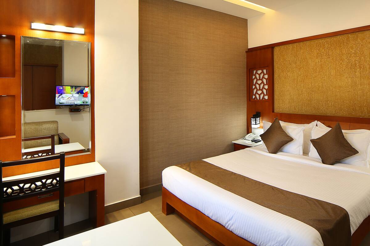 A hotel room with a bed, a desk with a chair, a television, and a ceiling fan.