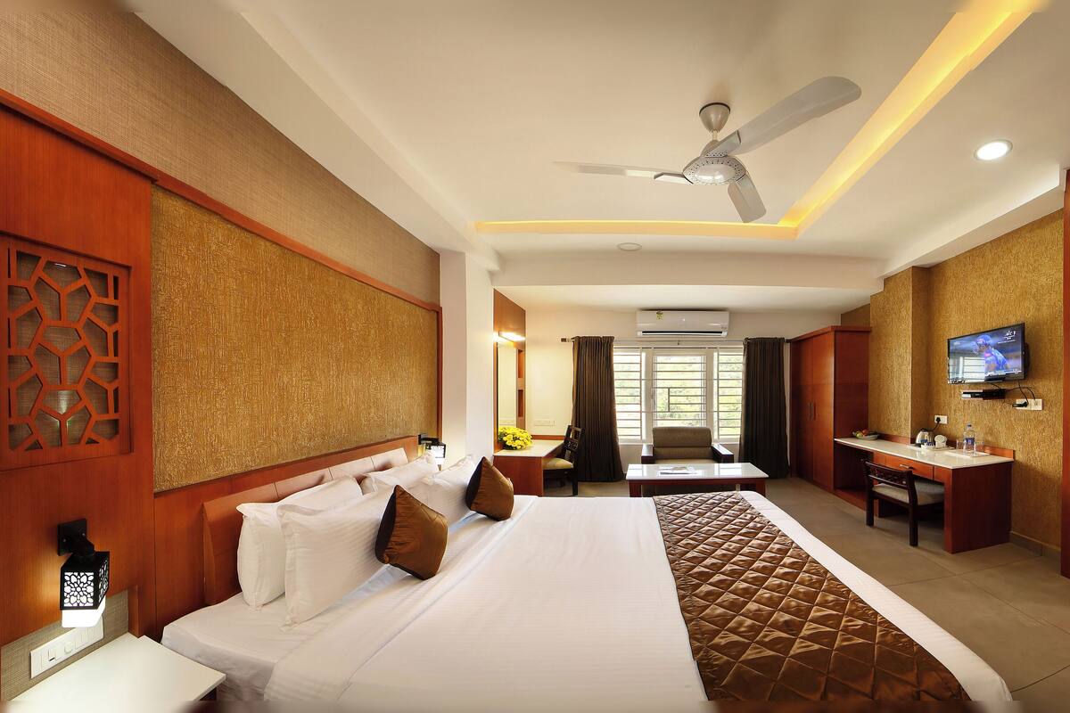 A hotel room with a bed, desk, chair, TV, and a ceiling fan.
