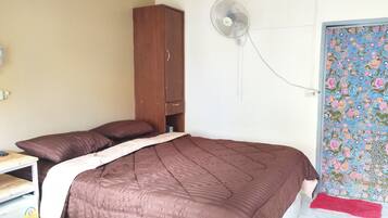 Un dormitorio con cama, armario, ventilador y puerta con papel tapiz floral.