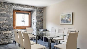 A conference room with a glass table, white chairs, a stone wall, a window, and a painting on the wall.