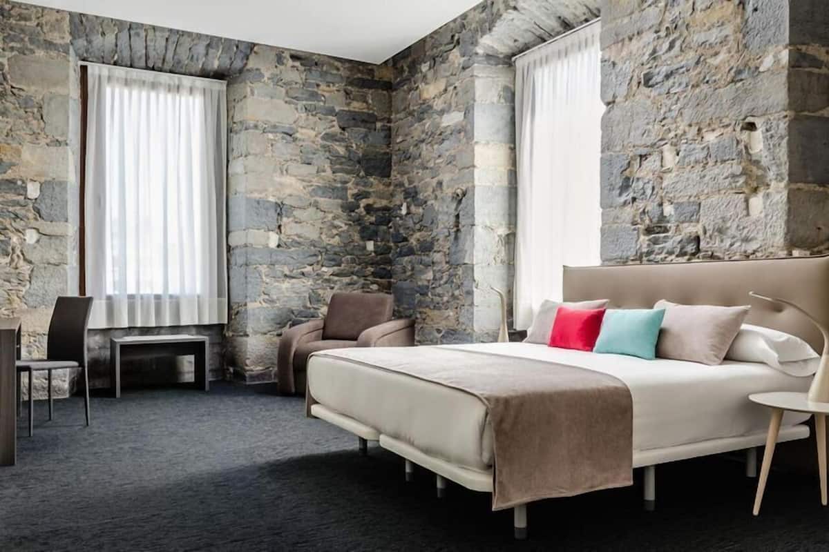 Une chambre avec un mur en pierre, un lit avec des oreillers, une chaise et une petite table.