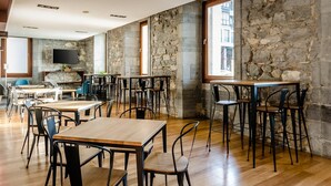 Un comedor amplio con mesas y sillas de madera, paredes de piedra y un gran ventanal que proporciona luz natural.