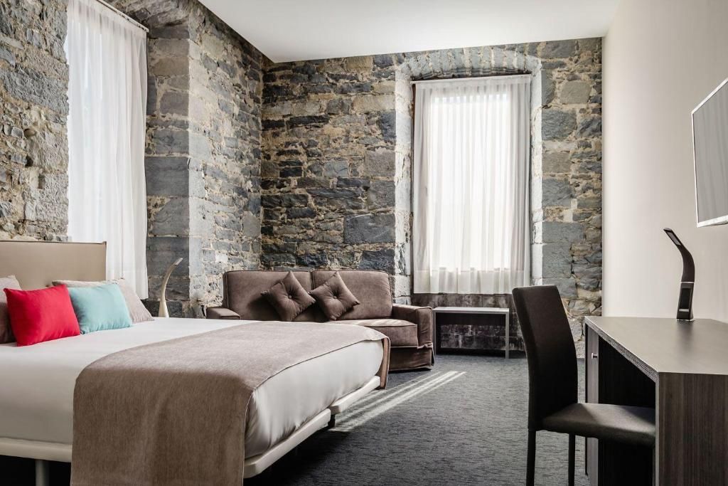Een hotelkamer met een stenen muur, een bed, een bank, een bureau en een stoel.
