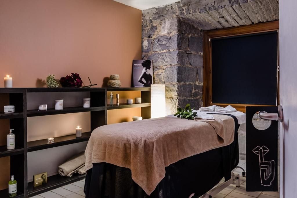 A spa room with a massage table, shelves with candles and toiletries, a stone wall, and a blackboard.
