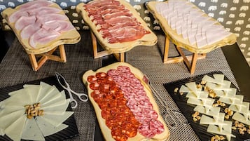 A variety of meats and cheeses displayed on wooden boards and plates, with a patterned background.