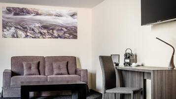 Habitación de hotel con sofá, escritorio y silla, televisor montado en la pared y un cuadro de un río.