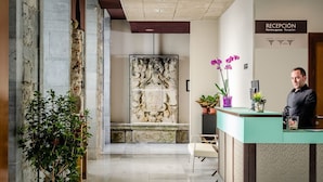 Zona de recepción de un hotel con pared de piedra, mostrador y un banco.