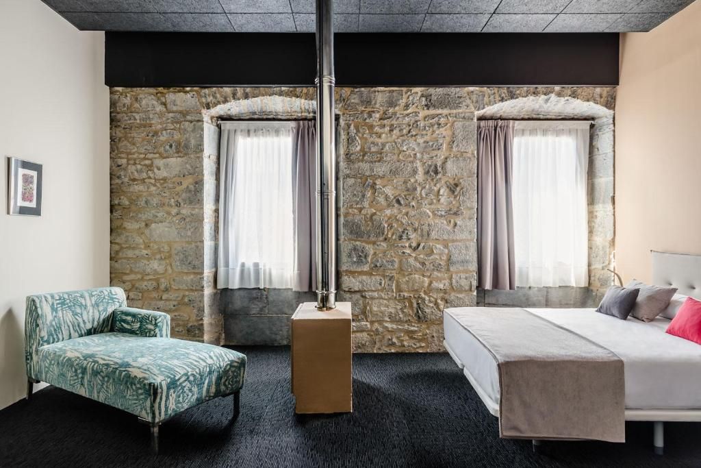 Habitación de hotel con pared de piedra, una cama, una silla y un pilar grande.