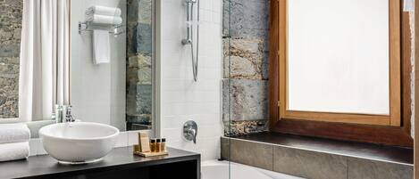 A modern bathroom with a stone accent wall, a large mirror, a white sink, and a shower area.