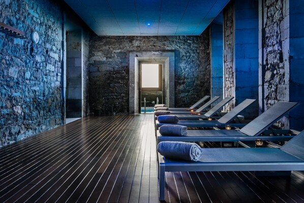 A spa room with stone walls, wooden flooring, and sun loungers with towels. - Hotel Balneario Orduña Plaza (Orduna)