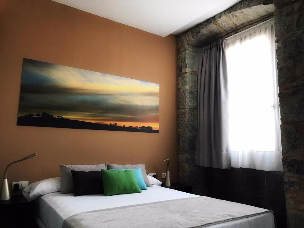 Habitación de hotel con una cama grande, un cuadro de una puesta de sol, una pared de piedra y una ventana con cortinas.