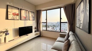 A modern living room with a flat-screen TV, a sofa, and a large window offering a city view. - Spacious Saigon (Ho Chi Minh City)