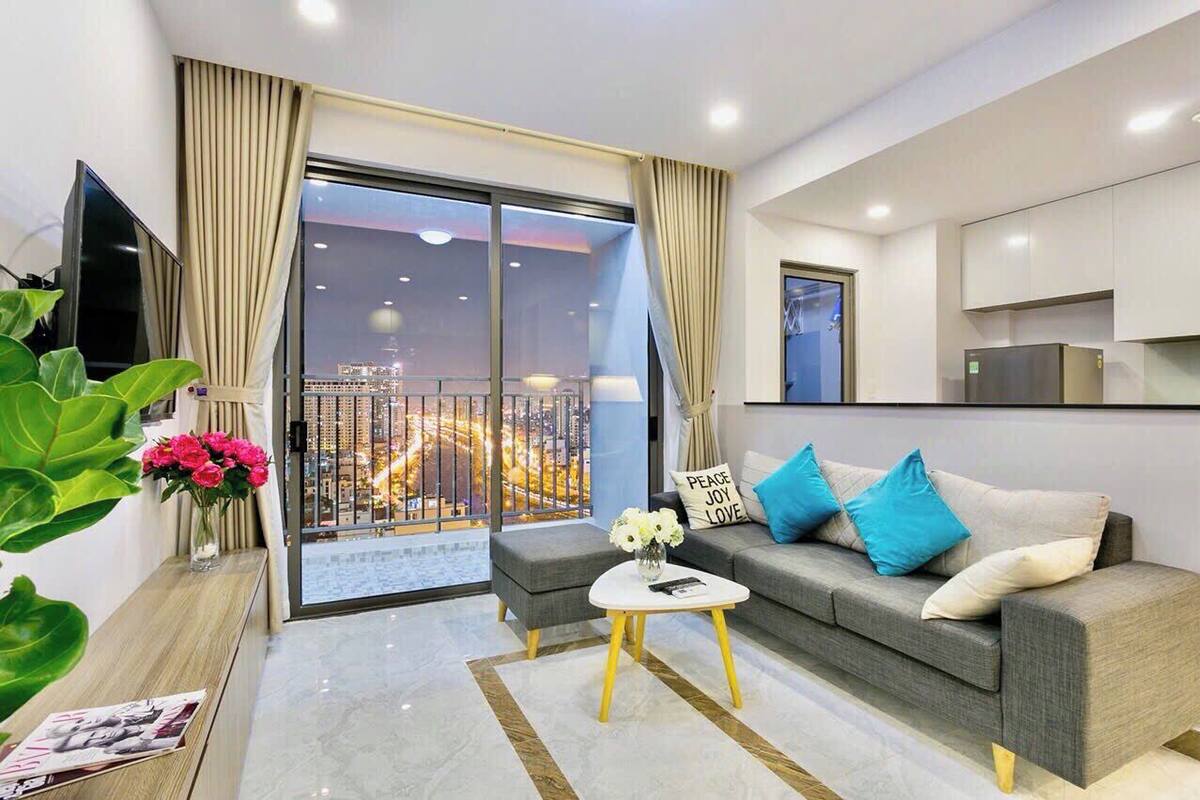 Ein modernes Wohnzimmer mit Sofa, Couchtisch, Flachbildfernseher, einem Balkon mit Stadtblick und einer Küchenzeile.