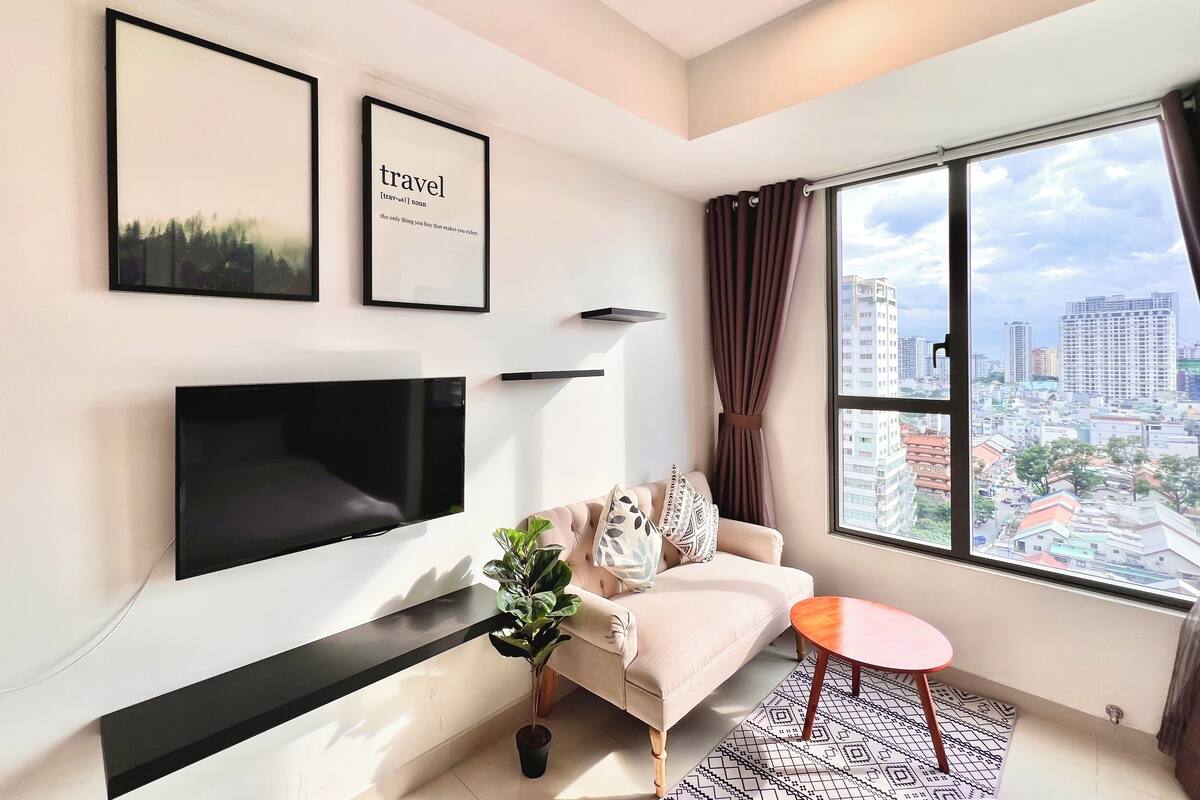 Ein modernes Wohnzimmer mit Flachbildfernseher, einer Couch, einem kleinen Tisch und einem großen Fenster mit Blick auf die Stadt.