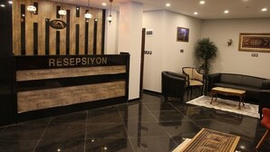 A reception area with a wooden reception desk labeled "RESEPSIYON," a black leather sofa, a small round table, and a potted plant. - Hotel Minerva Pazar (Pazar)