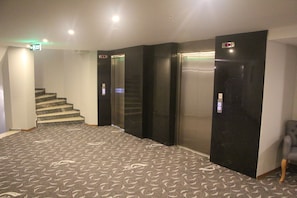 A hotel lobby with a carpeted floor, a staircase, and three elevators. - Hotel Minerva Pazar (Pazar)