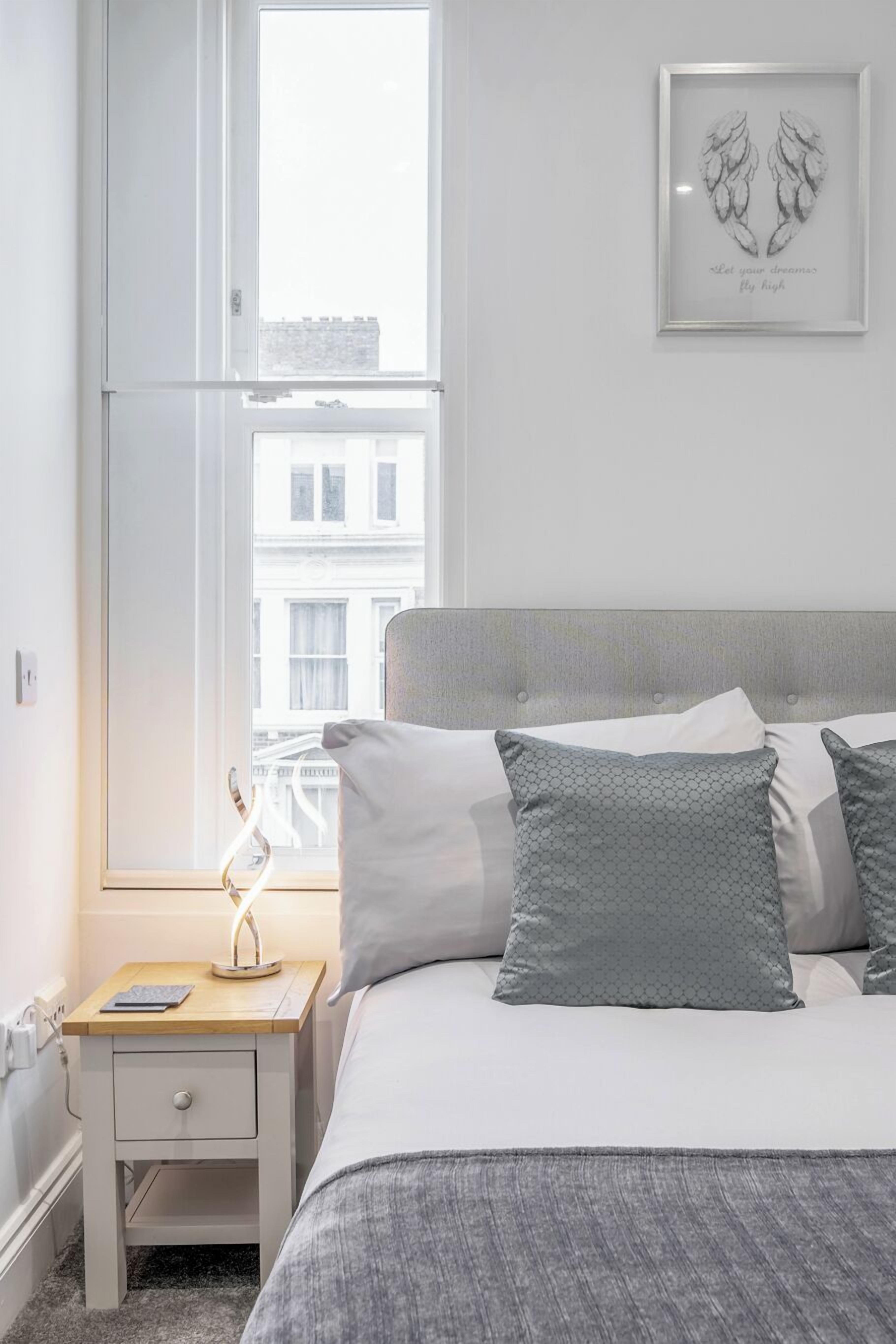 A neatly arranged bedroom with a bed, bedside table, and a framed artwork on the wall.