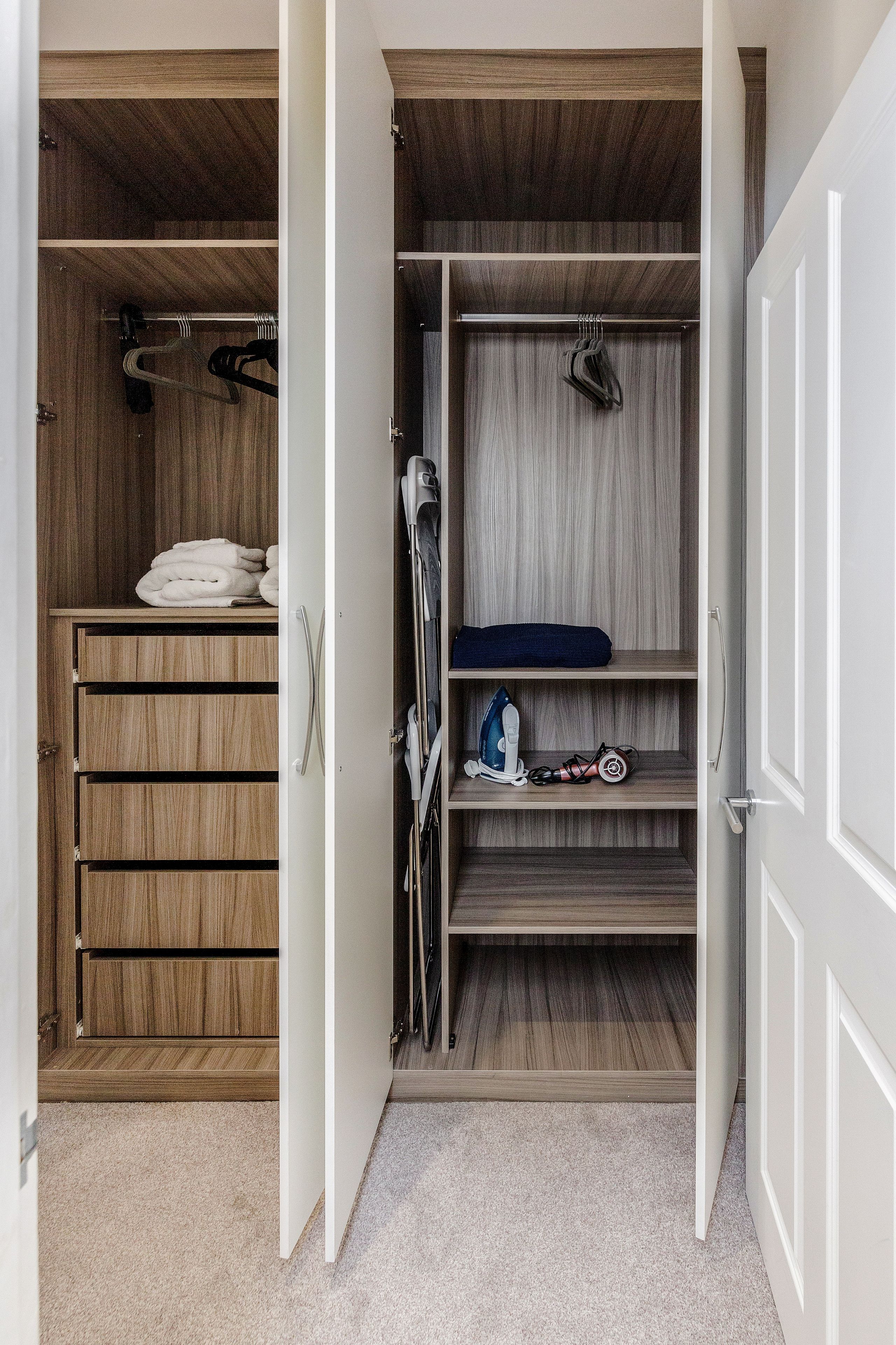 A walk-in closet with wooden shelves and hanging space, featuring neatly folded towels and a blue towel on the top shelf.