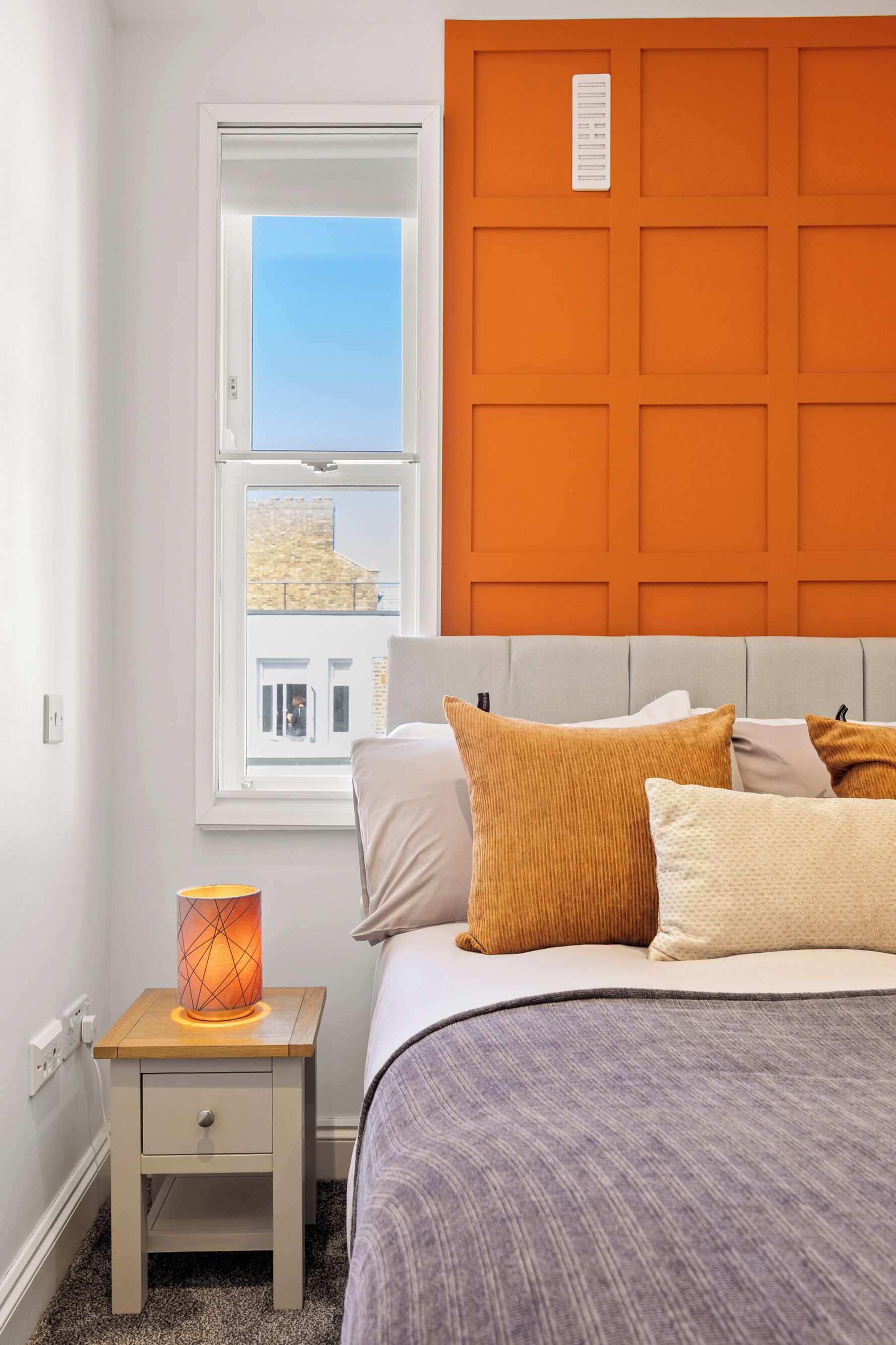 Un dormitorio con una cama, una mesita de noche, una ventana y un cabecero naranja.
