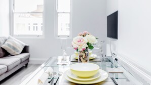 A modern dining area with a glass table, yellow plates, and a vase of flowers. - 2 Bedroom Portobello Notting Hill Apartment (London)