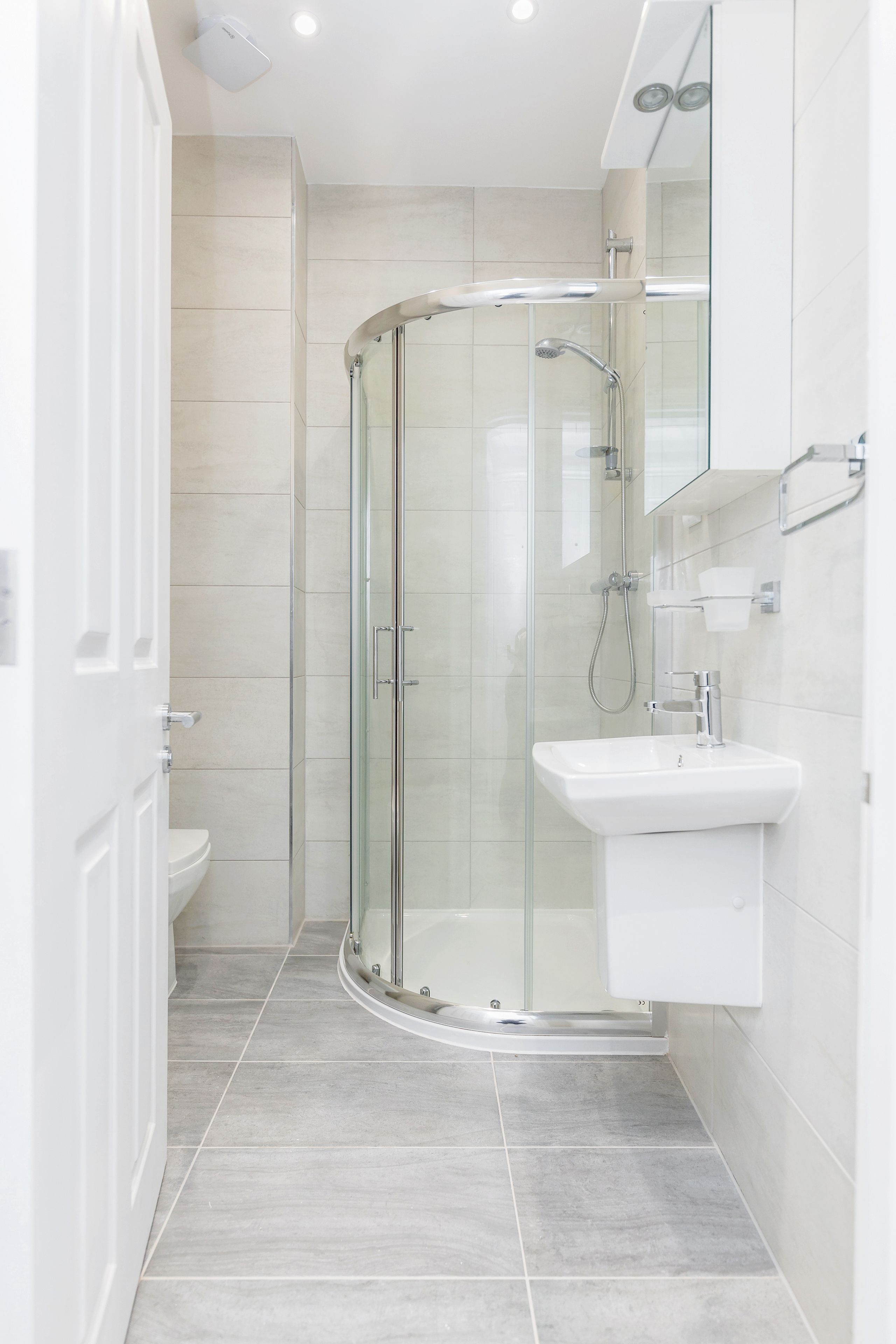 A modern bathroom with a glass-enclosed shower, a white sink, and a mirror above it.