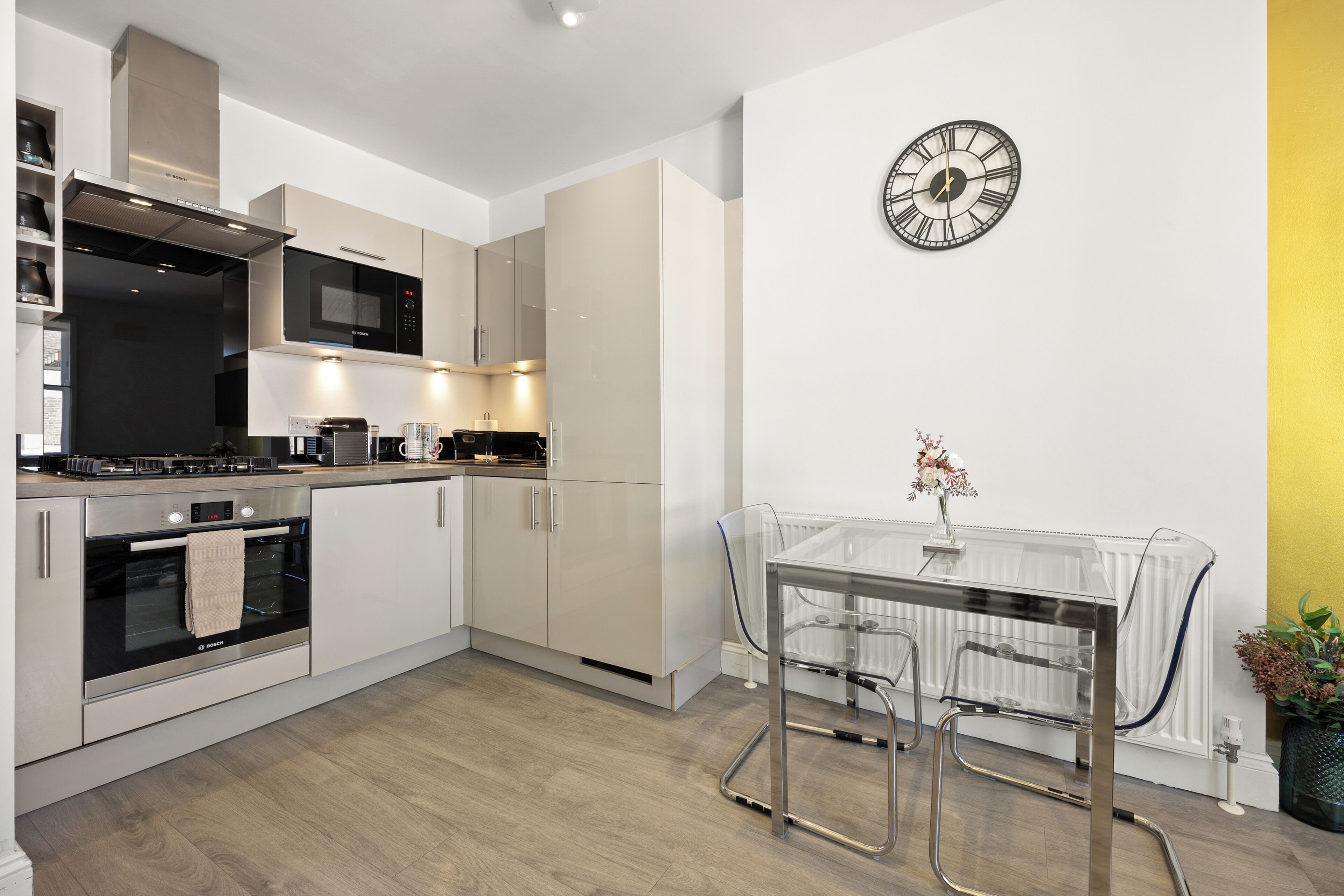 A modern kitchen with stainless steel appliances, a dining area with a glass table, and a wall clock.