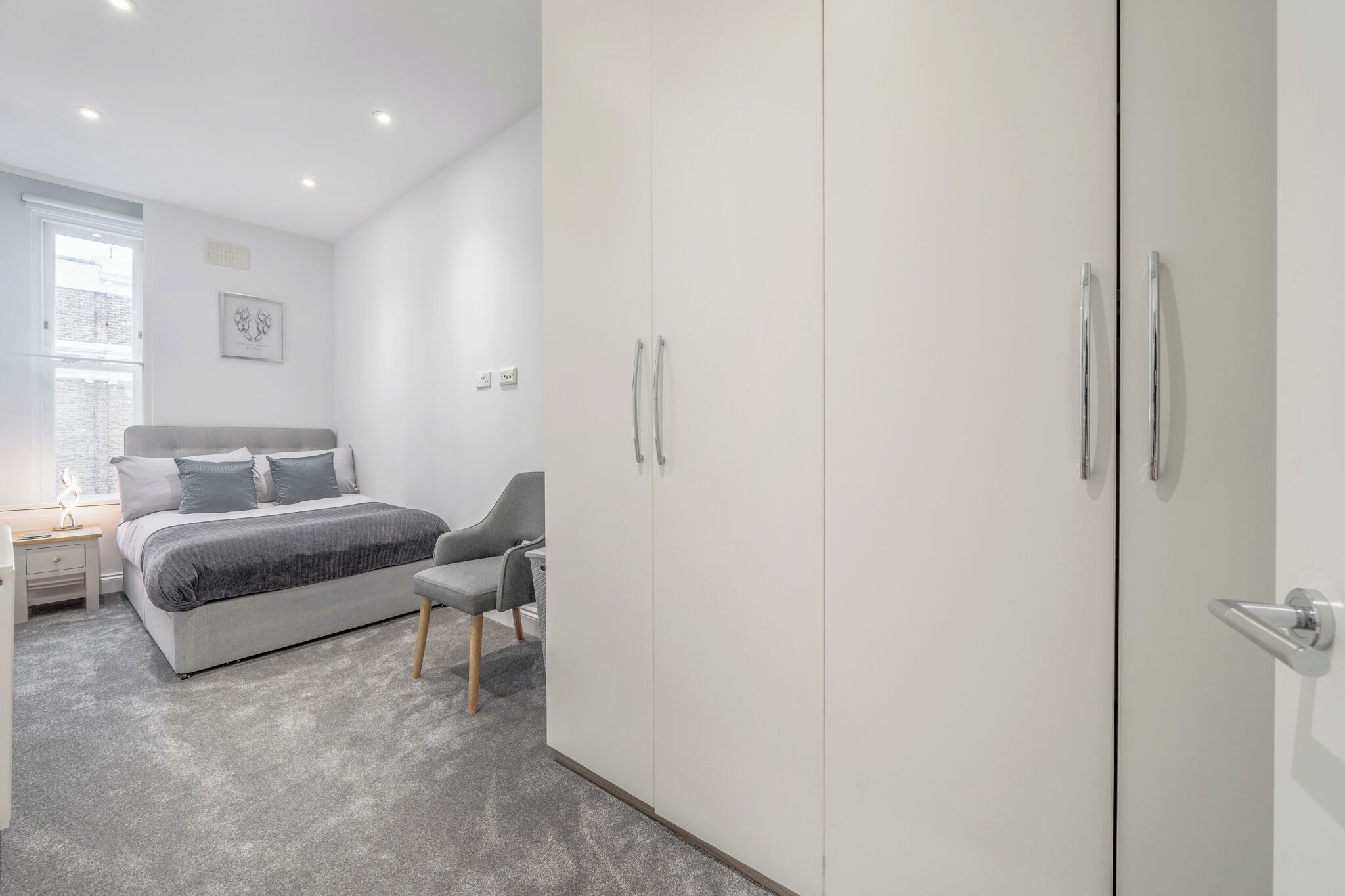 A modern bedroom with a bed, a chair, a wardrobe, and a nightstand.