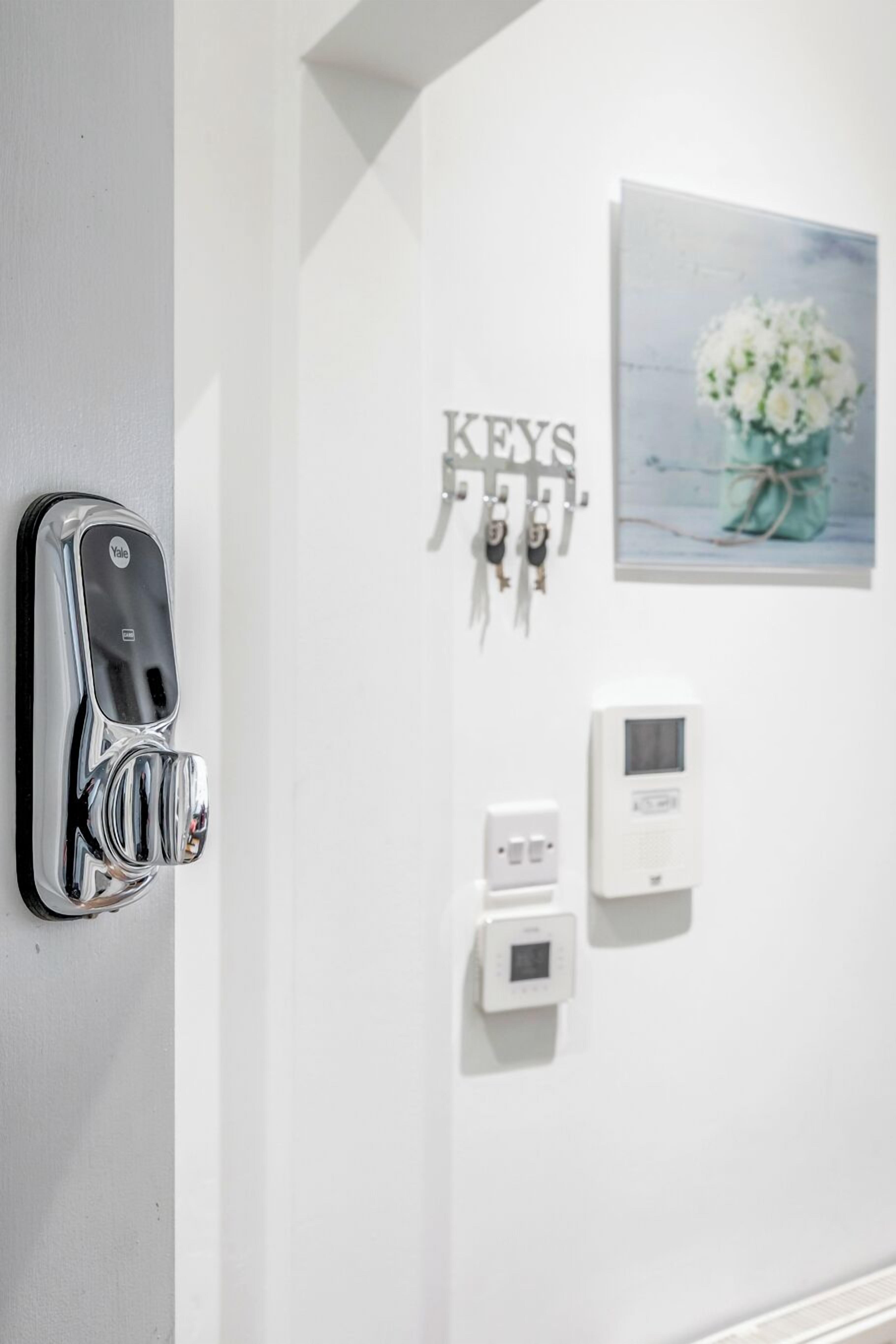 A wall-mounted Yale keyless entry lock, a set of keys, a thermostat, and a framed picture of flowers.