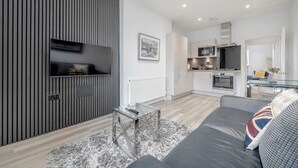A modern living room with a grey sofa, a glass coffee table, and a TV mounted on a wooden panel wall. - 2 Bedroom Portobello Notting Hill Apartment (London)